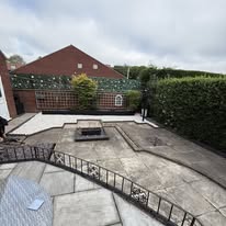 Before 1 A spacious outdoor area with paving, green hedges, and a fire pit.